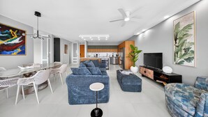 Un salon moderne avec un coin repas, une cuisine à l’arrière-plan et un grand téléviseur fixé au mur.