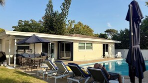 A poolside area with lounge chairs, a table, and an umbrella. - Serene 3-bedroom house with AC and saltwater pool in charming Clearwater. (Clearwater)