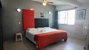 Ein Hotelzimmer mit Bett, Deckenventilator, Fenster mit Vorhängen und einem kleinen Hocker.