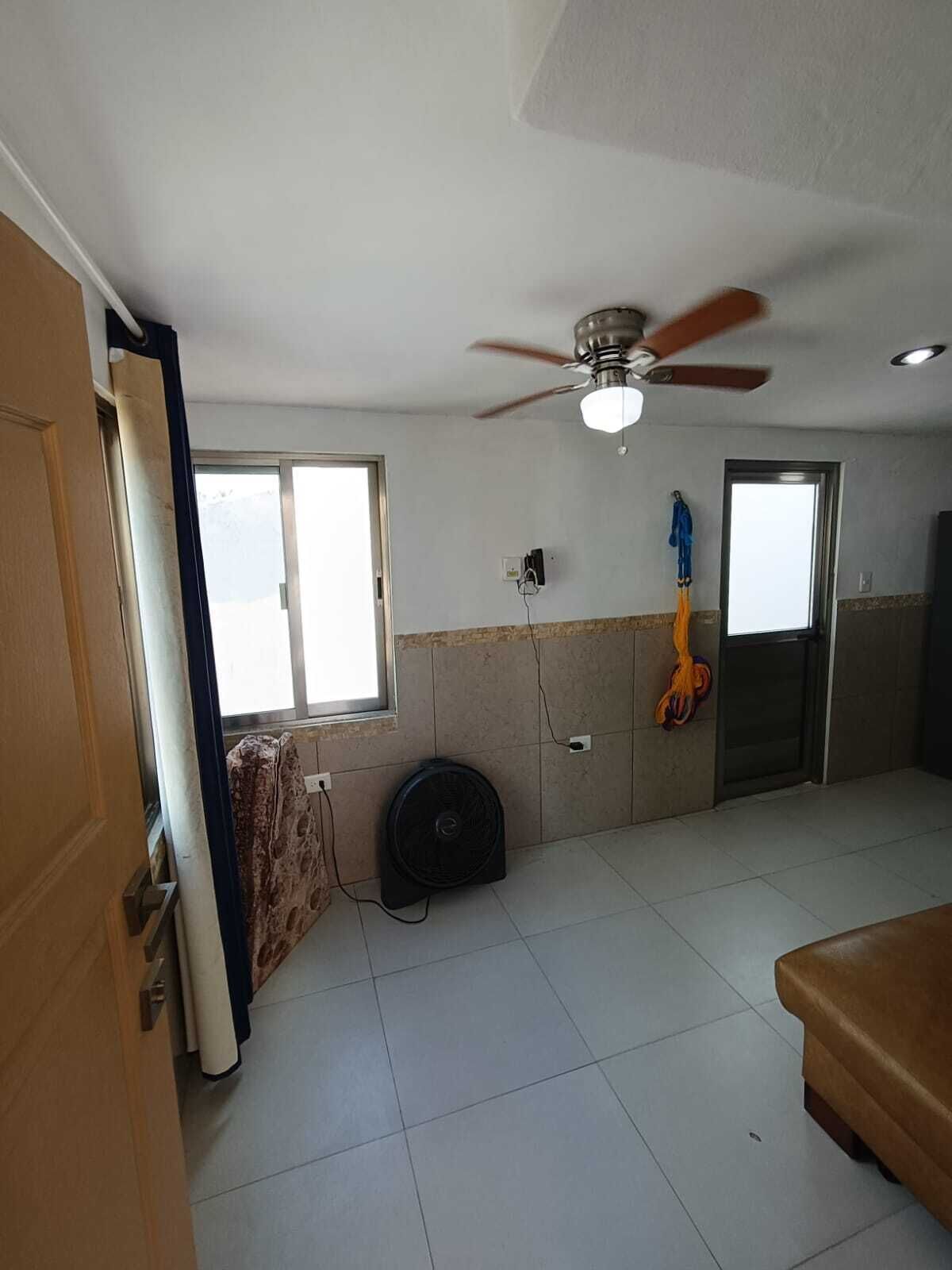 A room with a ceiling fan, two windows, a door, and a radiator.