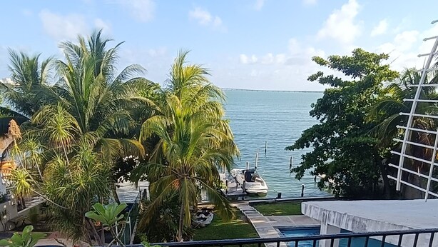 Ein Balkon mit Blick auf das Meer, Kübelpflanzen, ein Pool und ein in der Nähe liegender Bootssteg.