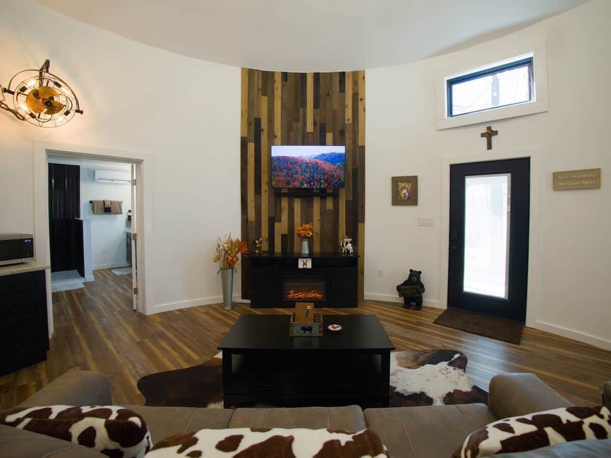 Uma sala de estar com lareira, televisão fixada numa parede de madeira, sofá e mesa de centro.