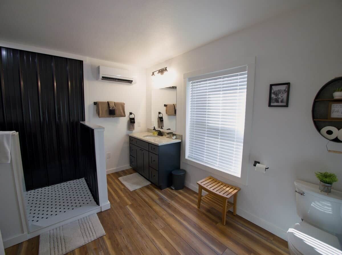 Un baño moderno con piso de madera, un lavamanos blanco, un espejo y un inodoro.