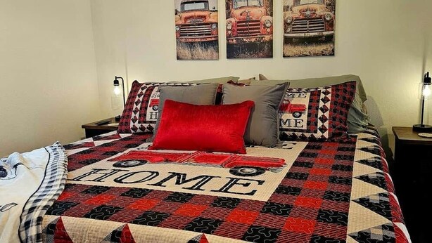 A bed with a quilt featuring a car and the word 'HOME,' two bedside lamps, and a wall with three car-themed paintings. - Silo Retreat (Sevierville)