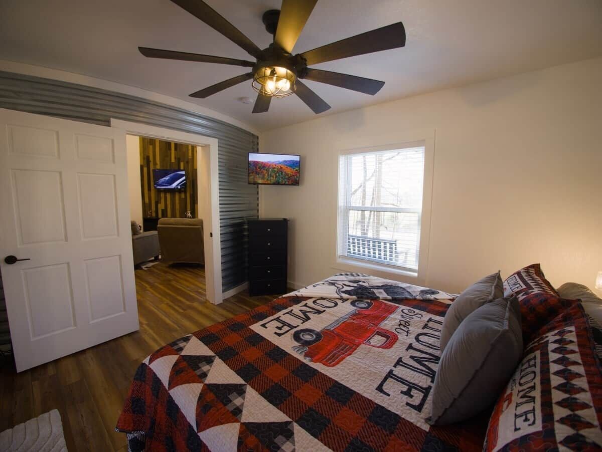 Ein Schlafzimmer mit einem Bett, einem Deckenventilator, einem Fernseher und einem Fenster.