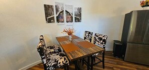 A dining area with a wooden table, cow-print chairs, and a refrigerator.