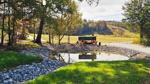 A rural road with a wooden bench and a cart, surrounded by trees and a small body of water. - Silo Retreat (Sevierville)