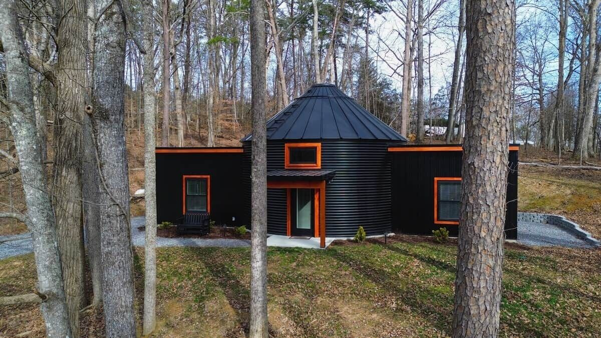 A cabin with a black exterior and orange trim, surrounded by trees.
