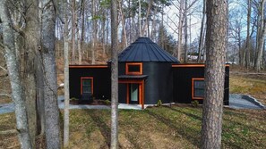 A cabin with a black exterior and orange trim, surrounded by trees.