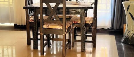 Una mesa de comedor con cuatro sillas, un par de gafas sobre la mesa y una lámpara a la derecha.