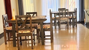 Un comedor con mesas y sillas de madera, una vela sobre una mesa, y vistas a través de cortinas traslúcidas.