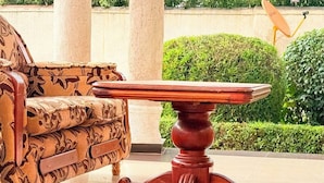 Una mesa de madera con base tallada, un sofá estampado y un jardín bien cuidado al fondo.