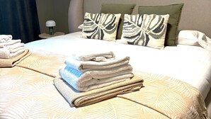 Una habitación de hotel con cama, almohadas, una mesita de noche, lámpara y toallas.