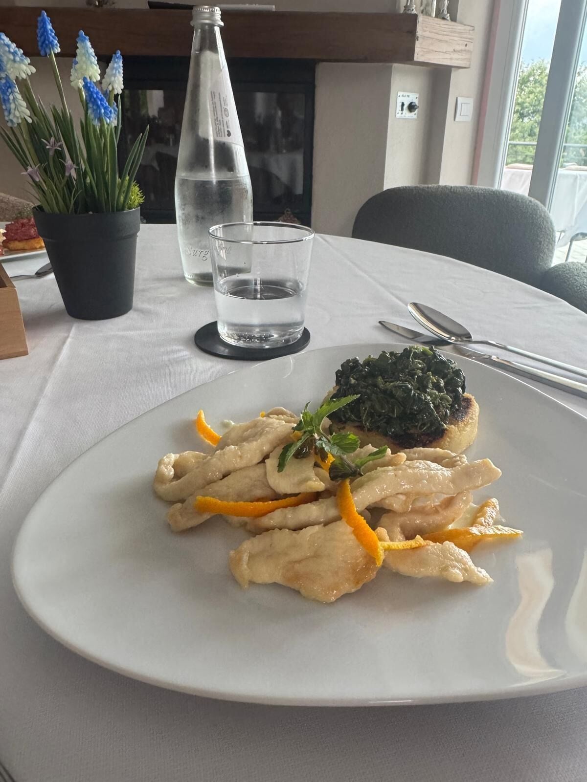 A dining table with a plate of food, a glass of water, and a potted plant.