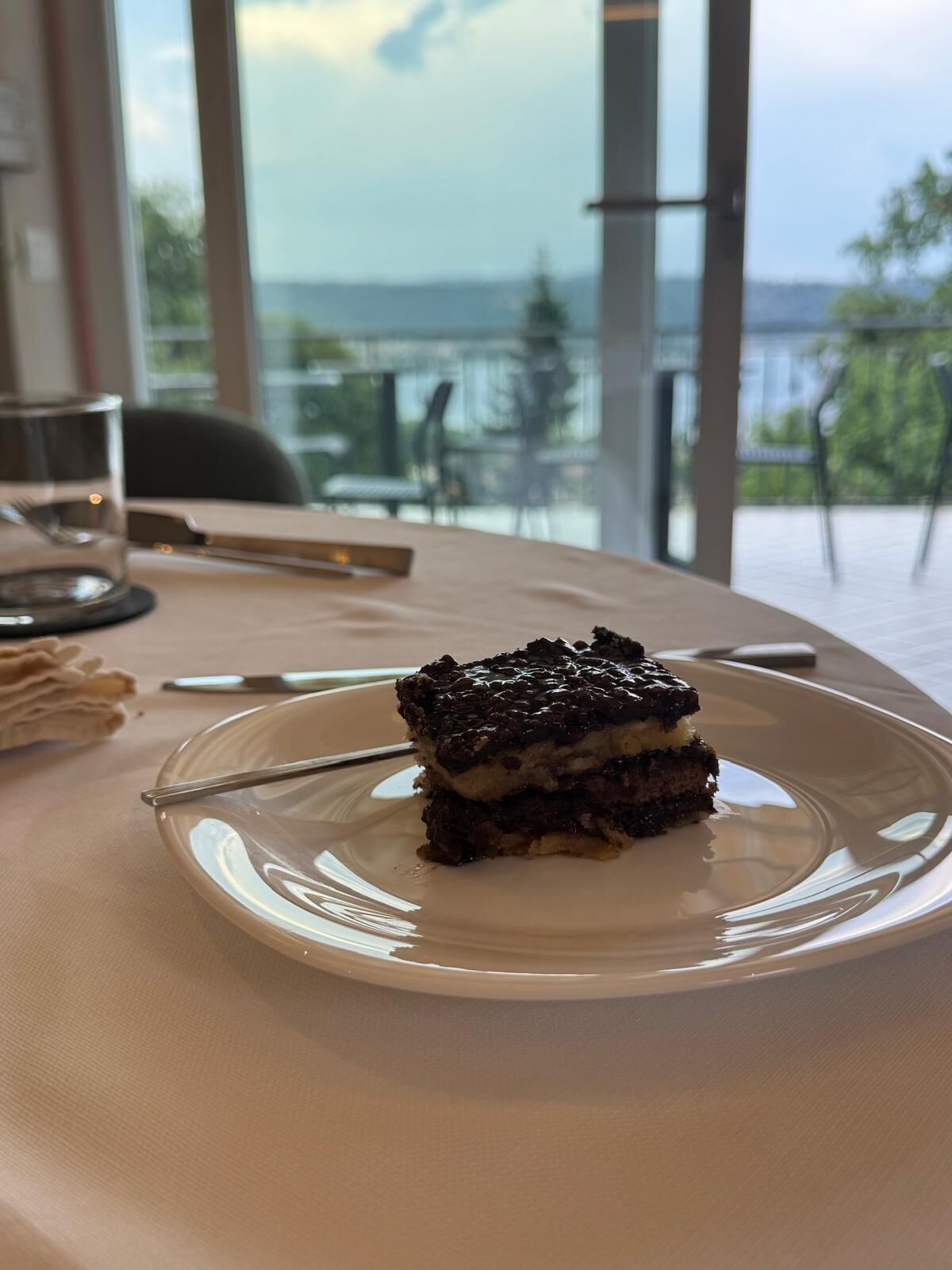 A slice of cake on a plate on a table with a view of the outdoors.