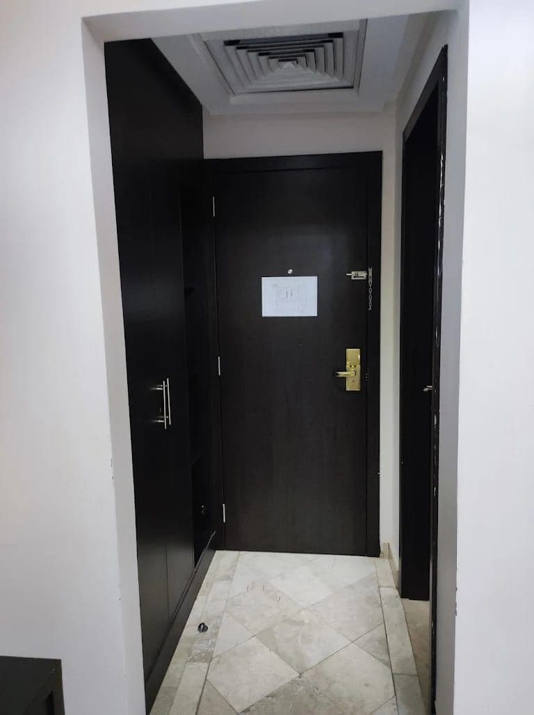 A narrow hallway with a dark door, a light switch, and a small sign on the wall.