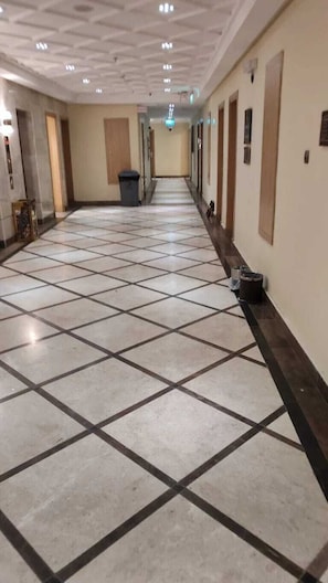Um corredor de hotel com piso de azulejos, portas e uma lixeira.