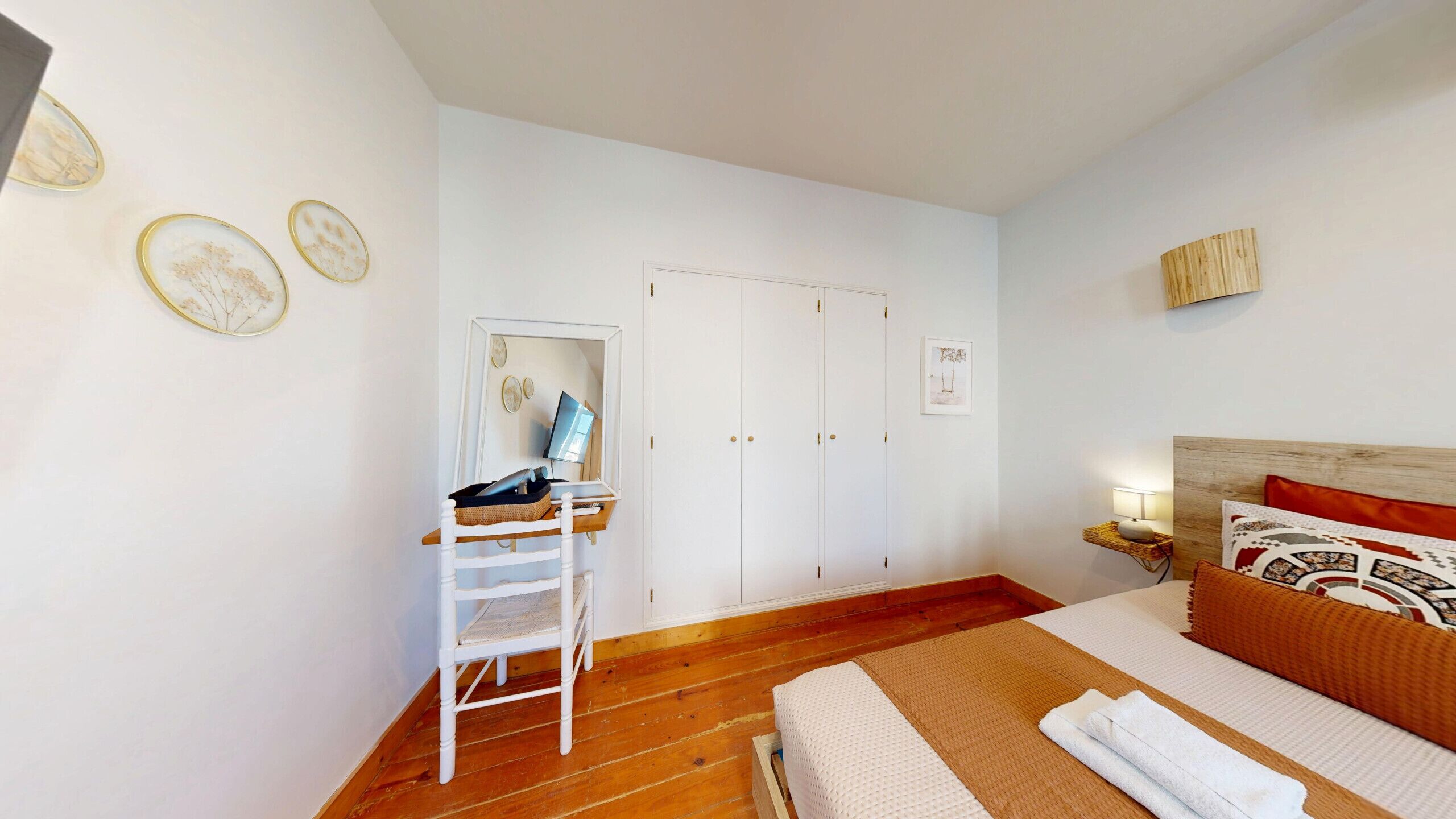 A bedroom with a bed, a desk with a chair, a wardrobe, and a mirror.