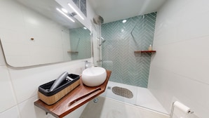 Une salle de bain moderne avec un grand miroir, un lavabo blanc, une douche et un mur orné d’un motif en chevrons.