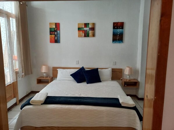 A bedroom with a large bed, two bedside tables with lamps, and three wall-mounted artworks.