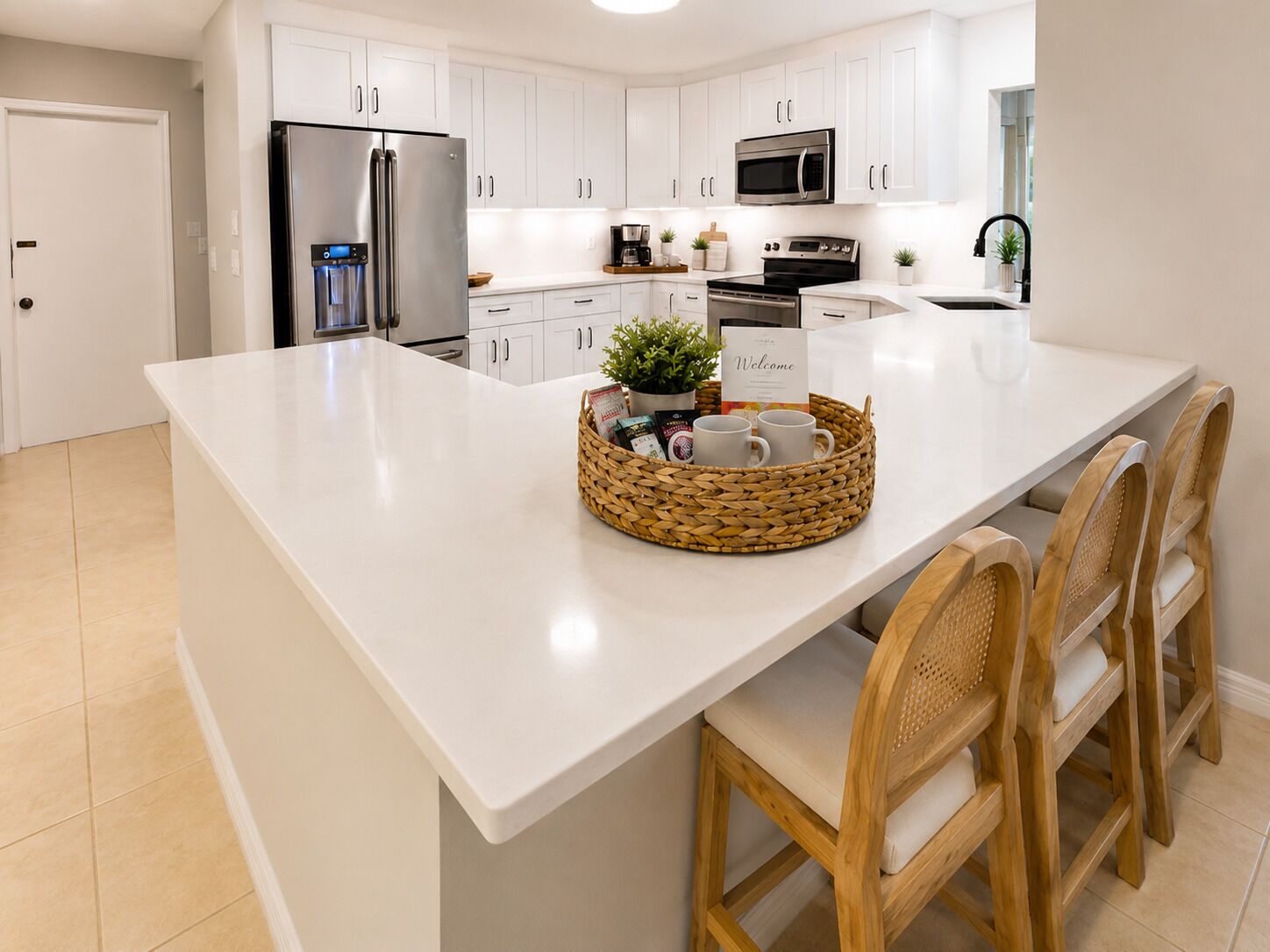 A modern kitchen with white cabinetry, stainless steel appliances, a central island with a woven basket, and wooden chairs.