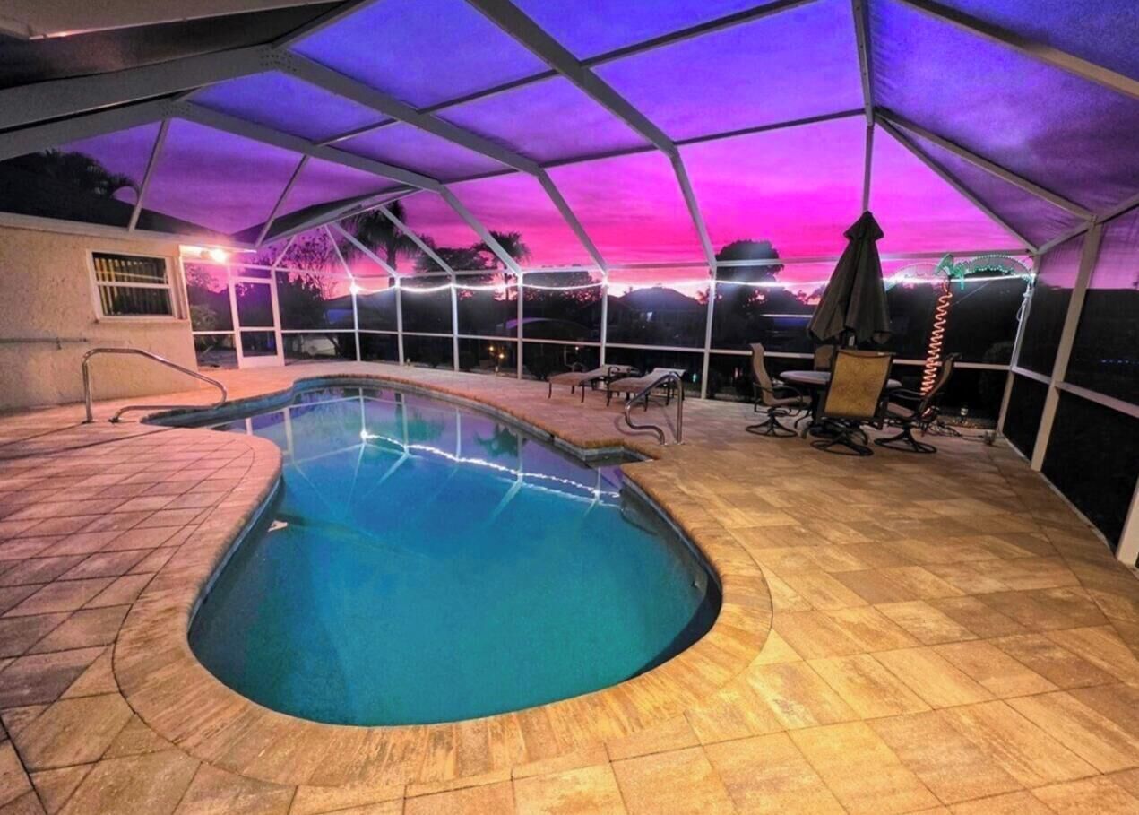 An indoor swimming pool with a curved edge, surrounded by a covered patio area with seating.