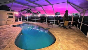An indoor swimming pool with a curved edge, surrounded by a covered patio area with seating.