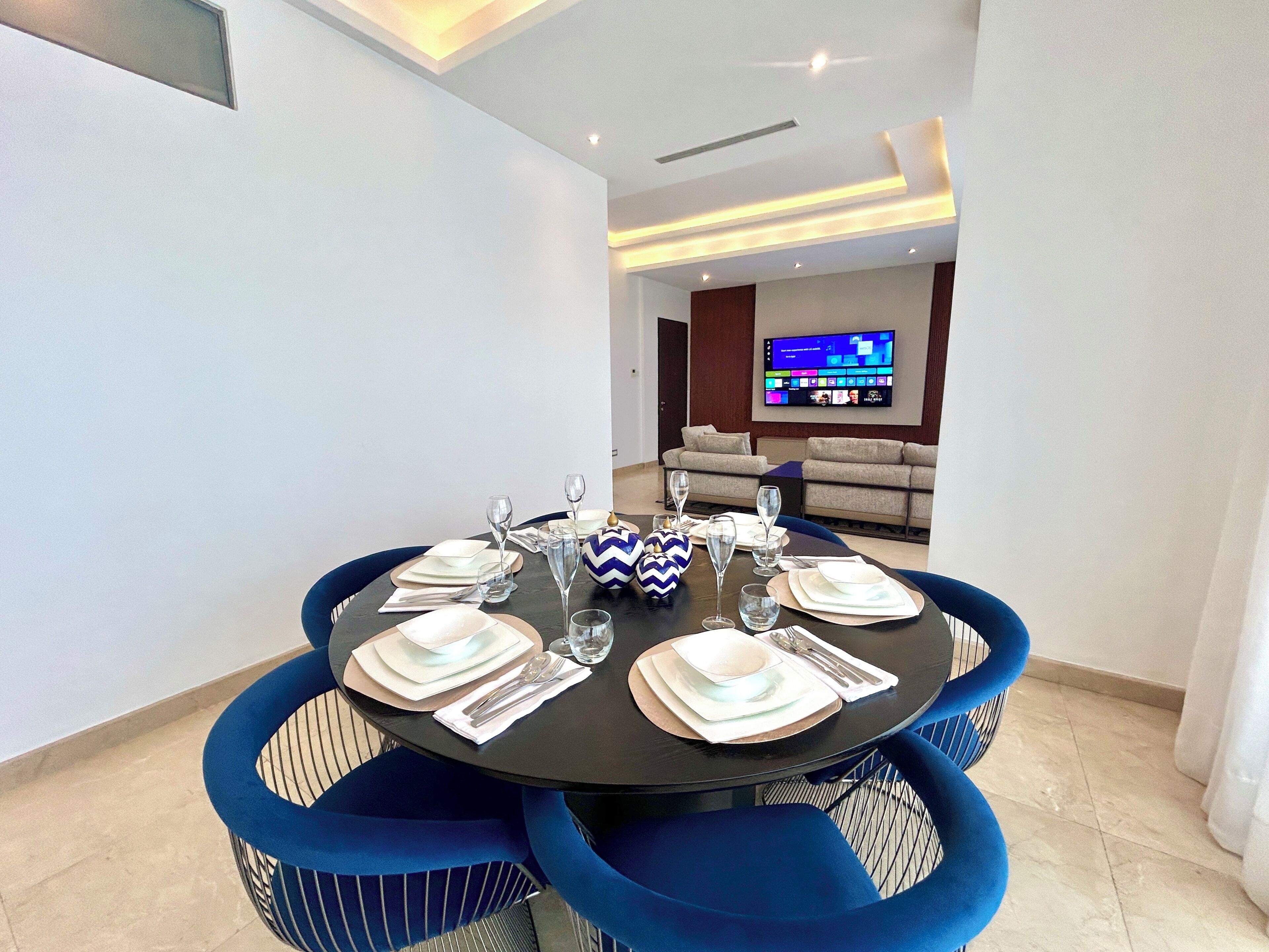 A dining area with a round table set for six, surrounded by blue upholstered chairs.