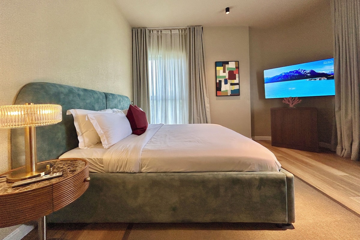 A hotel room with a bed, a TV, a lamp, and a painting on the wall.