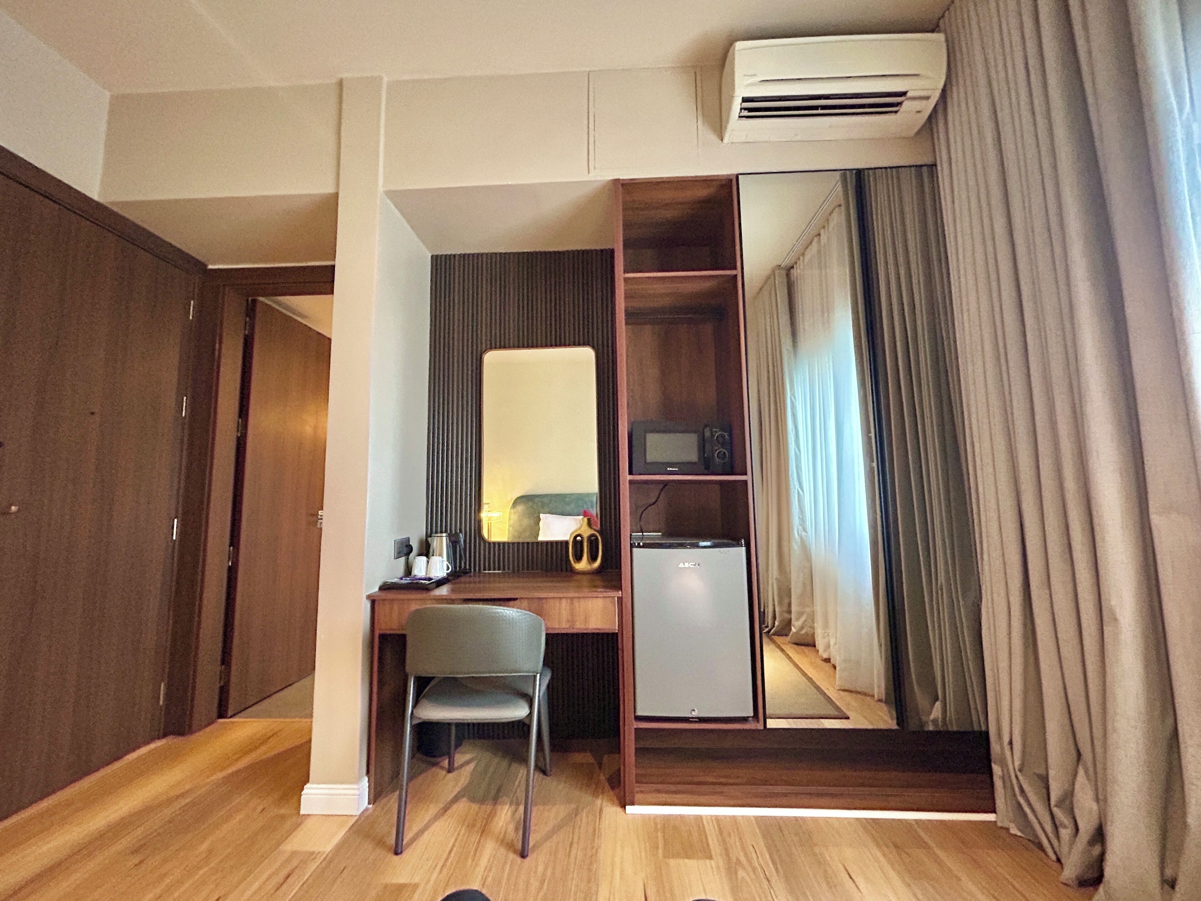 Une chambre d’hôtel équipée d’un bureau, d’une chaise, d’un miroir, d’une armoire et d’un petit réfrigérateur.