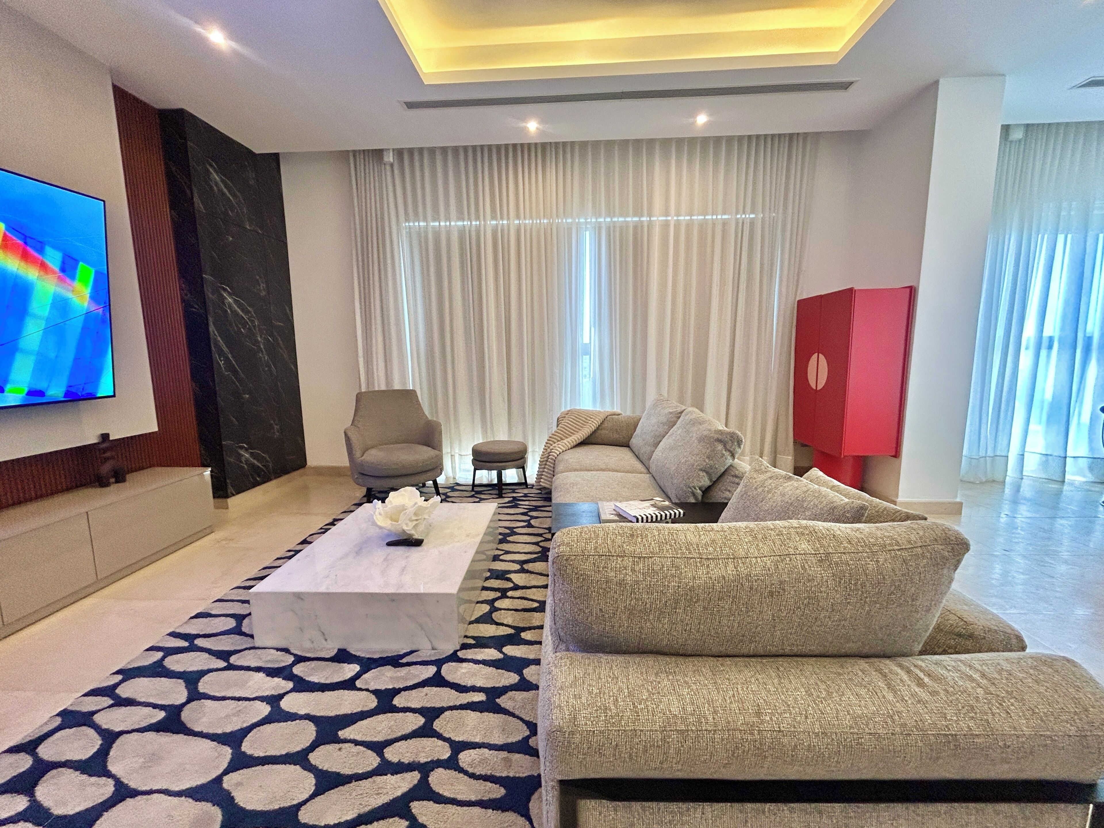 A modern living room with a sofa, armchair, coffee table, and a flat-screen TV mounted on the wall.