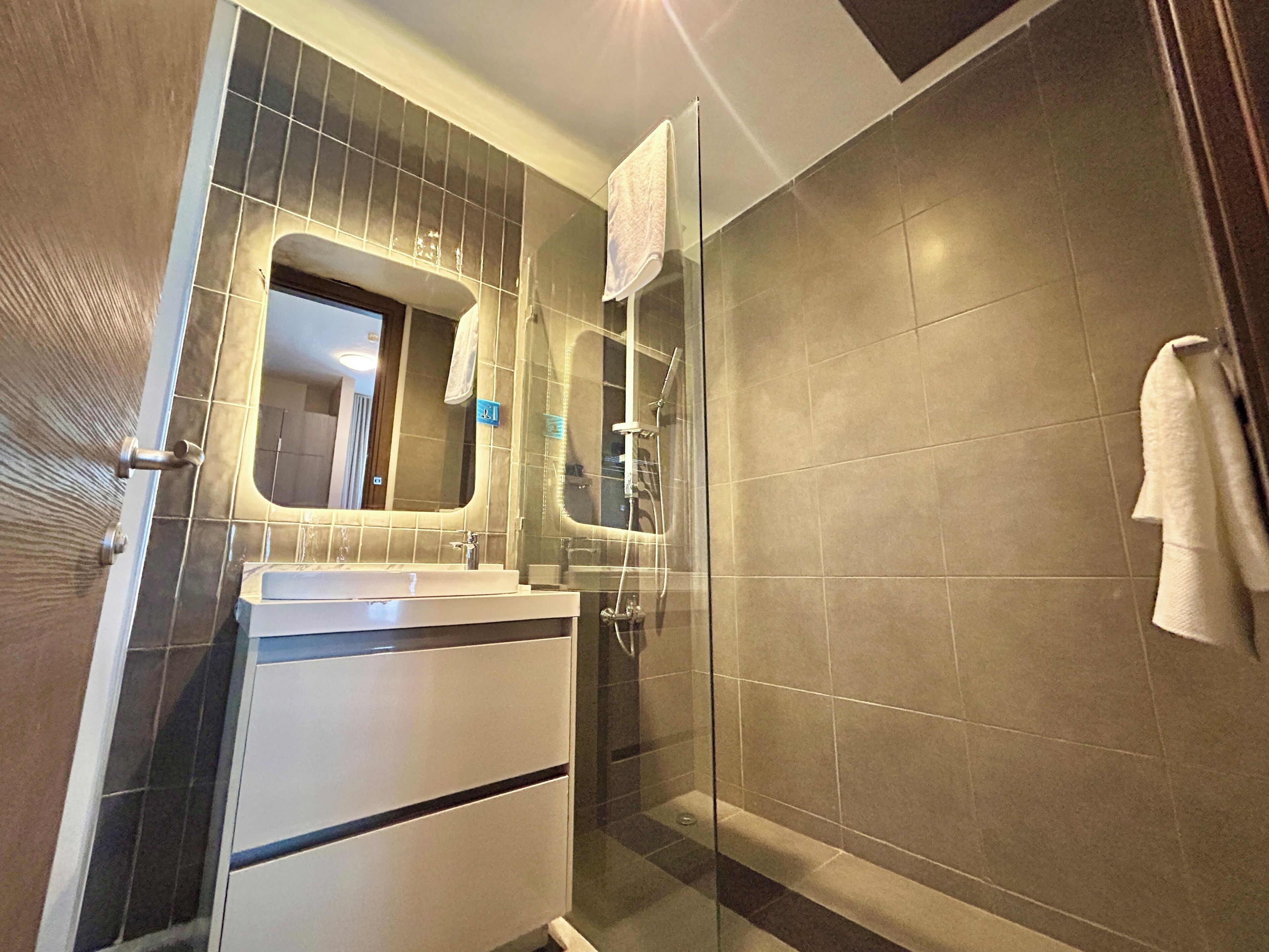 A modern bathroom with a glass shower enclosure, a sink with a mirror, and a towel rack.