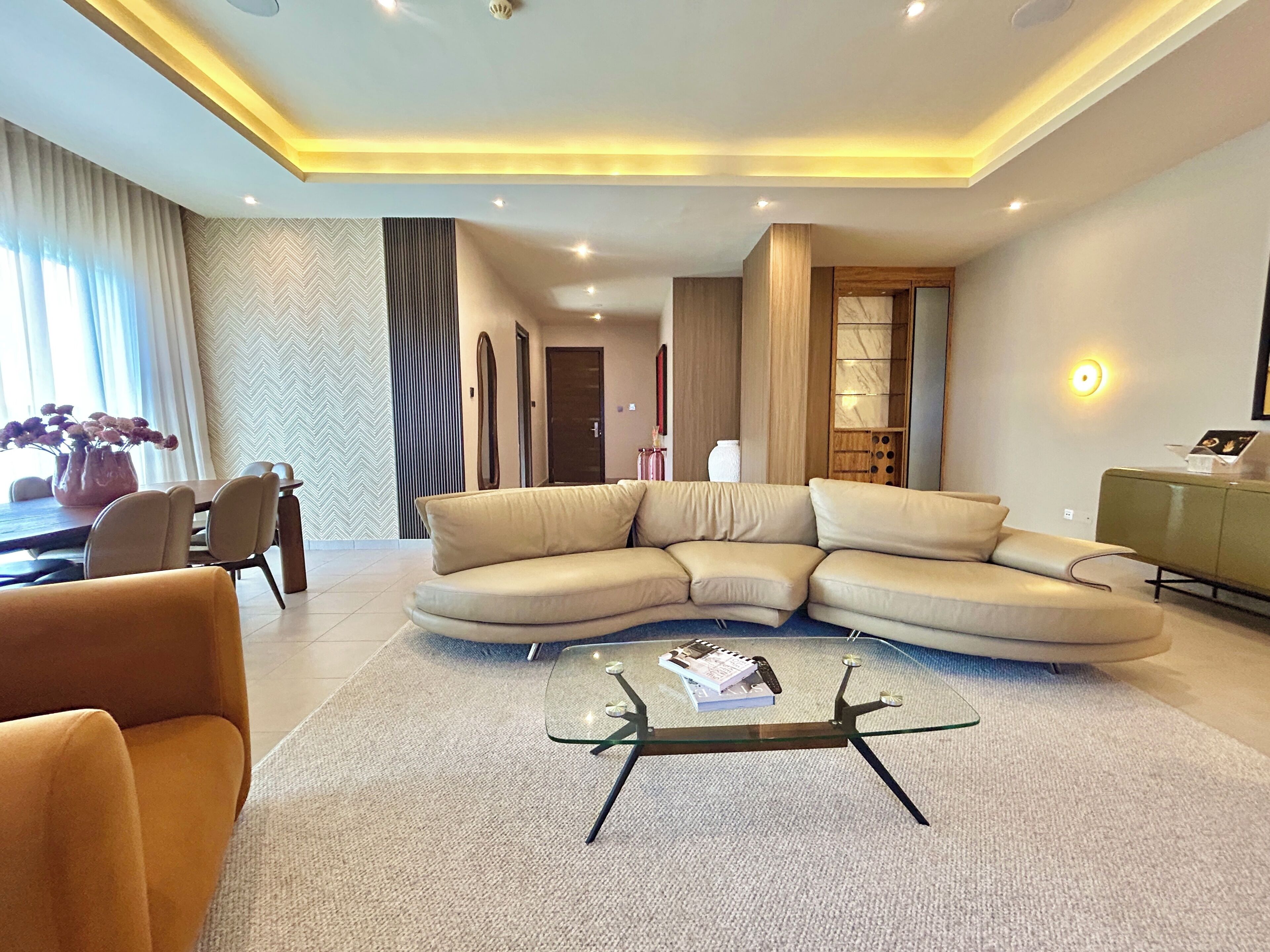 A modern living room with a sectional sofa, a glass coffee table, and a dining area with a table and chairs.