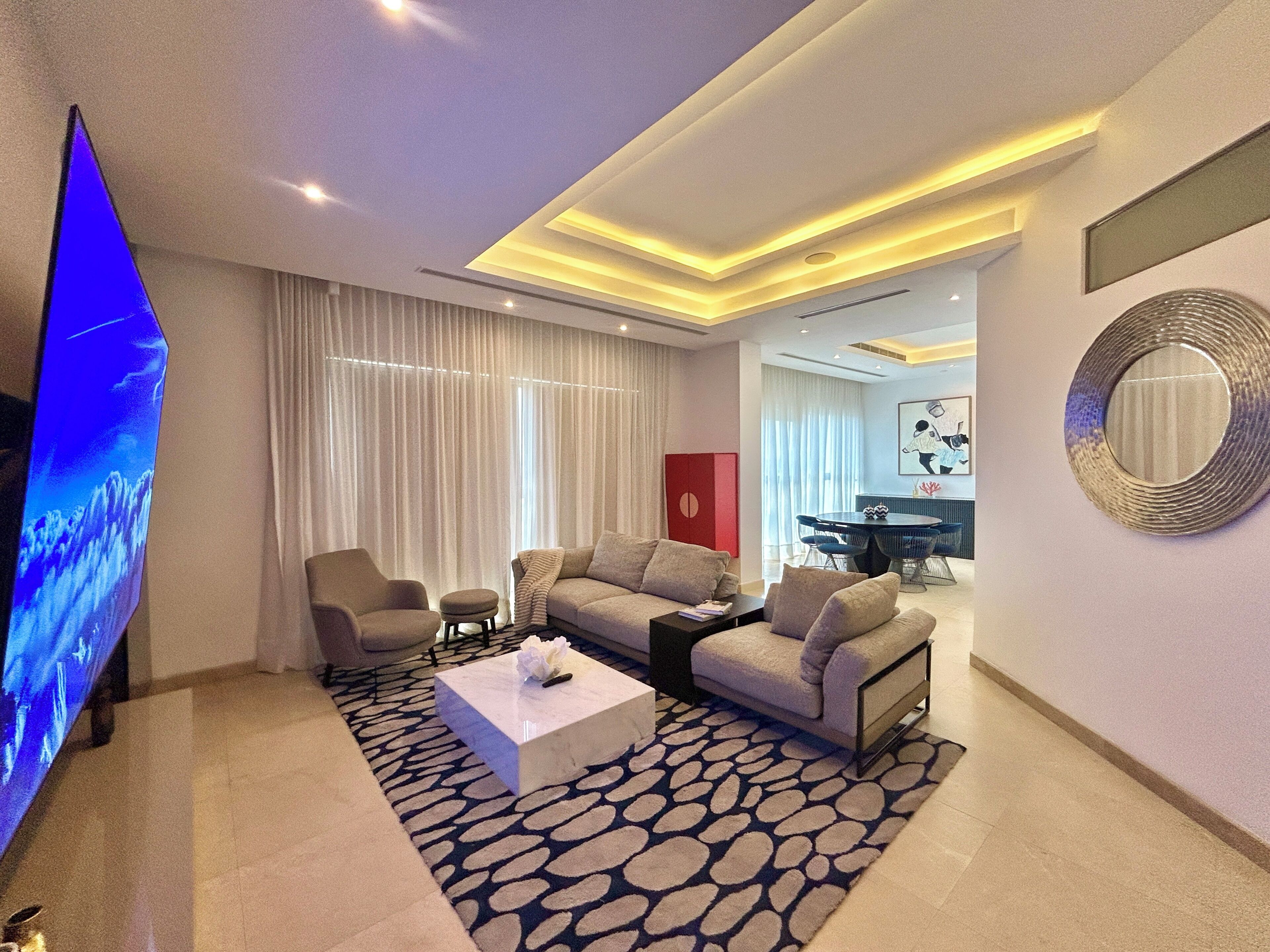Ein modernes Wohnzimmer mit Fernseher, Sofas, einem Couchtisch und einem Essbereich mit roter Akzentwand.