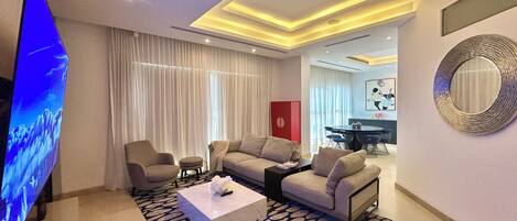 A modern living room with a flat-screen TV, sofas, a coffee table, and a dining area with a red accent wall.