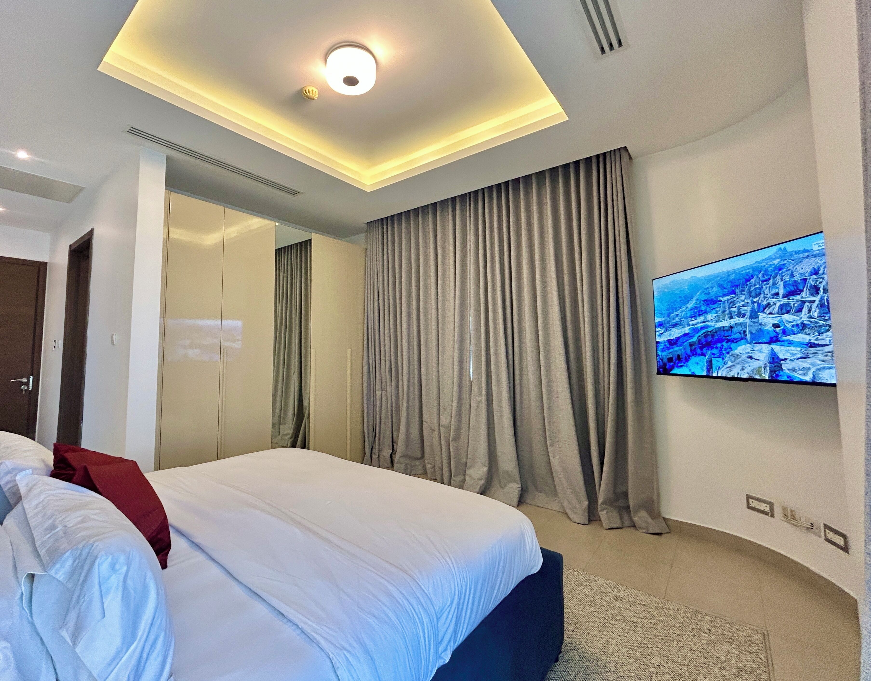 A modern hotel room with a bed, a TV mounted on the wall, and a ceiling light.