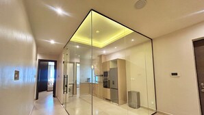 A modern interior with a glass partition, a kitchen area with appliances, and a hallway leading to another room.