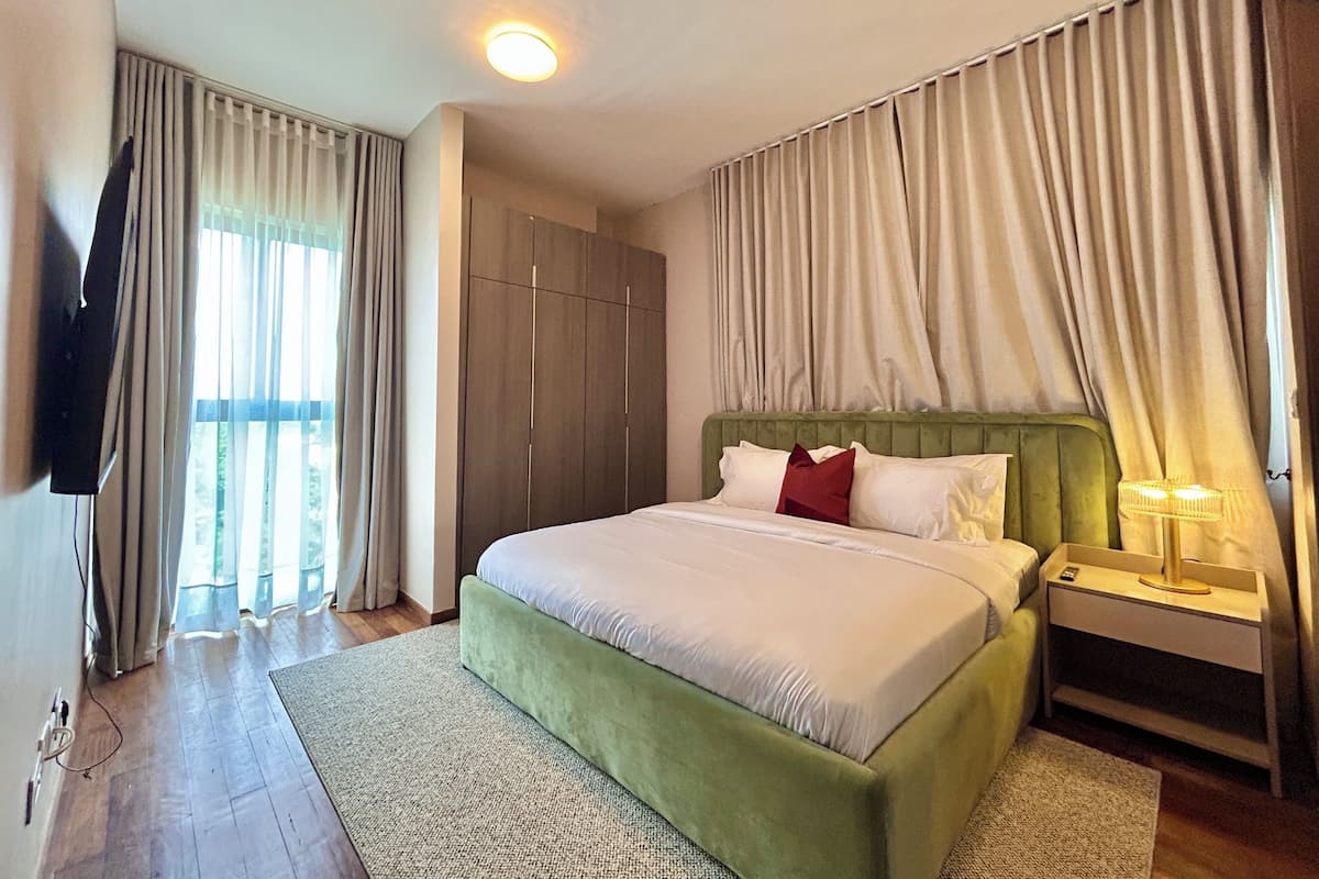 A hotel room with a bed, curtains, a TV, a bedside table with a lamp, and a wooden wardrobe.
