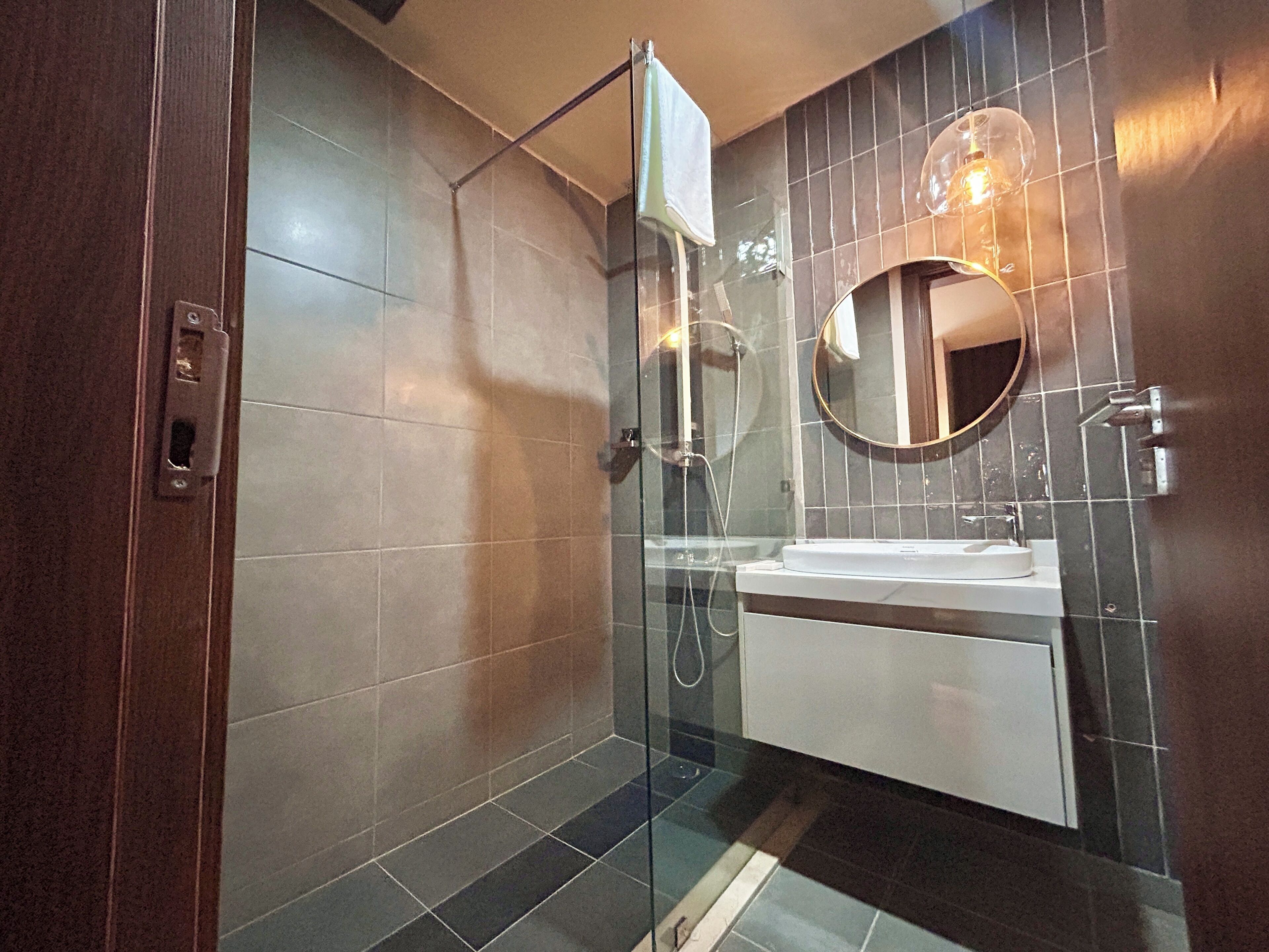 Un bagno moderno con doccia vetrata, un lavandino bianco e uno specchio rotondo.