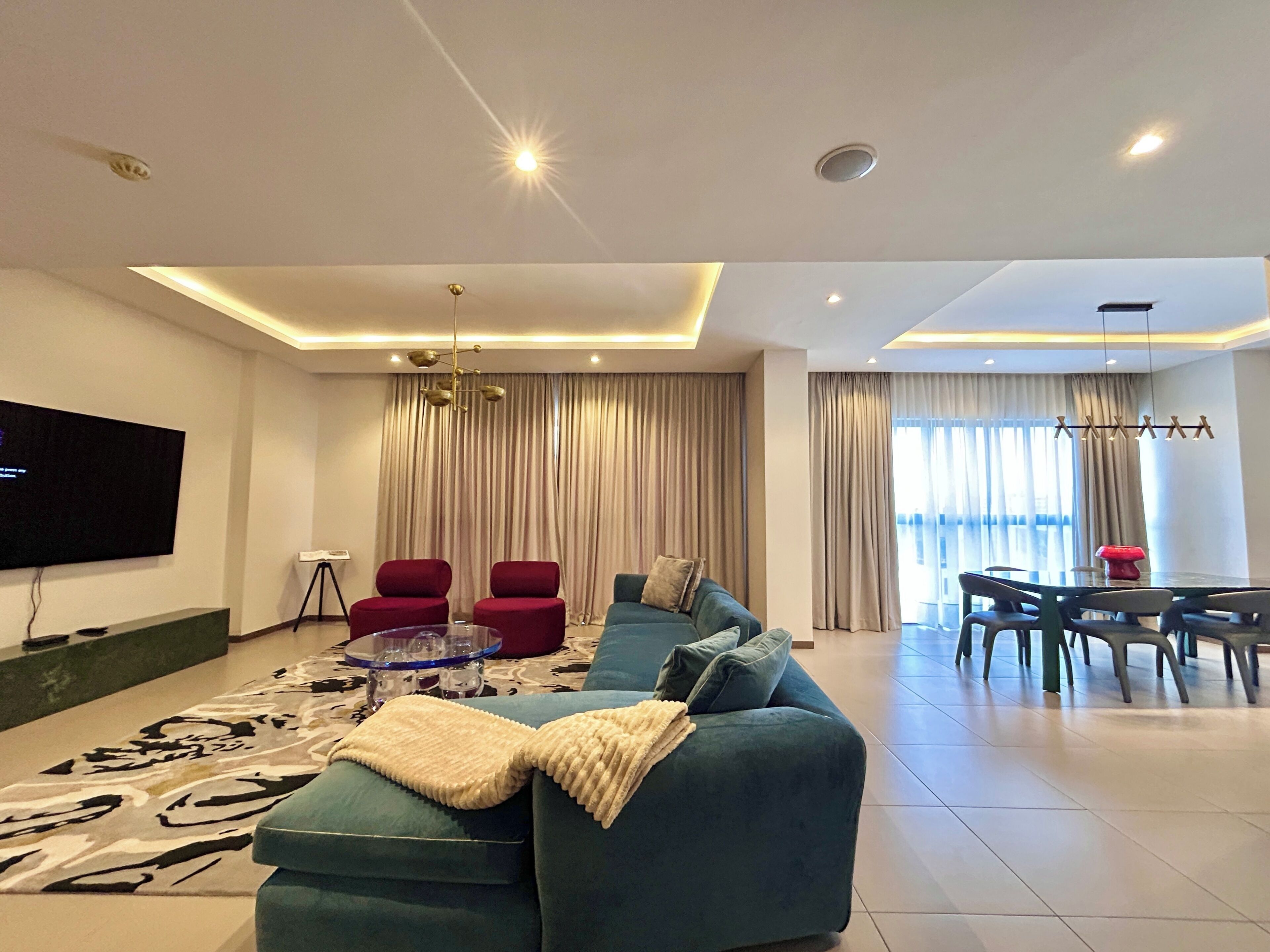 A modern living room with a sectional sofa, red chairs, a glass coffee table, and a flat-screen TV.