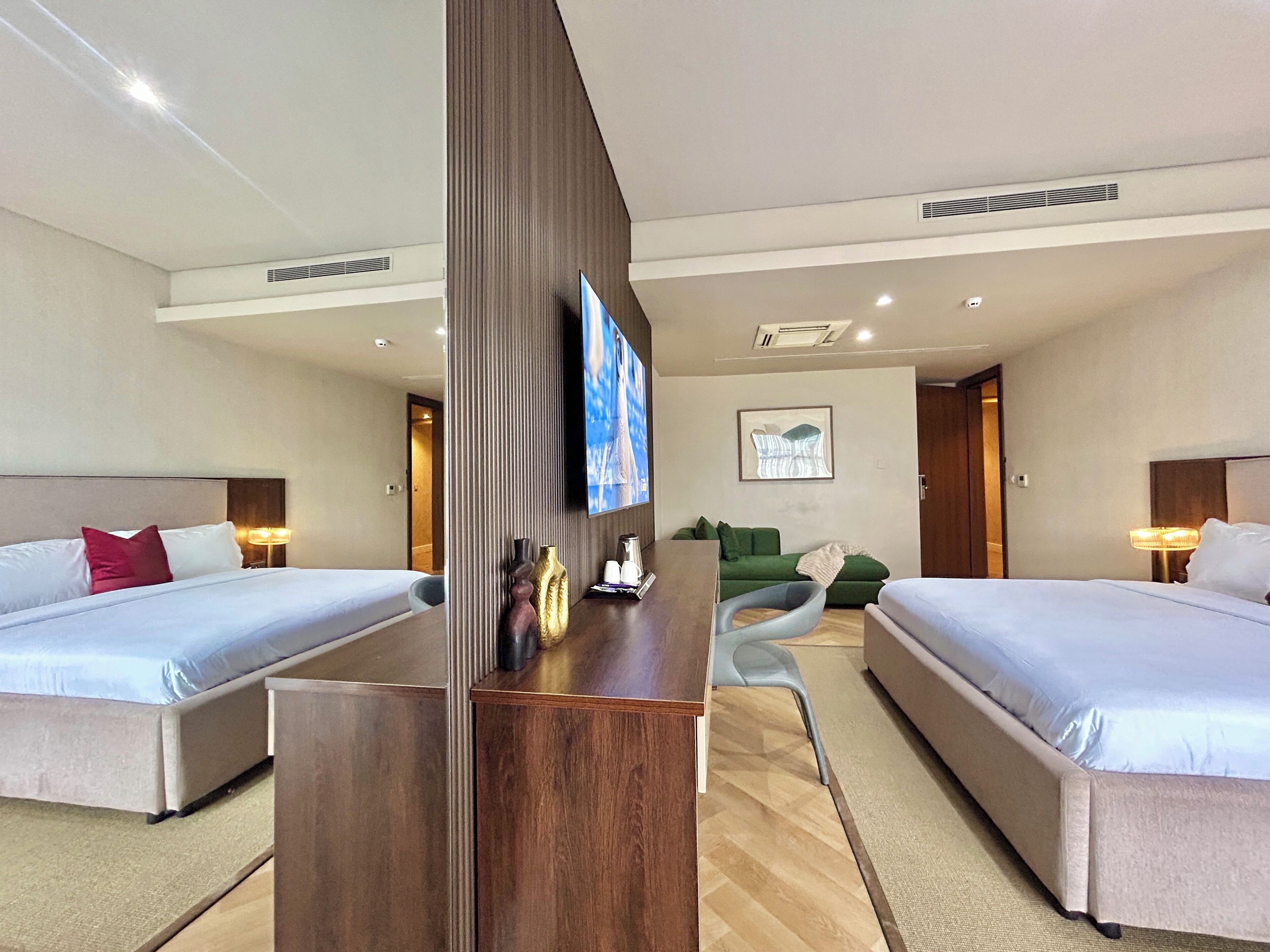 Habitación de hotel con dos camas, televisión, escritorio, sofá y puerta que da a otra habitación.