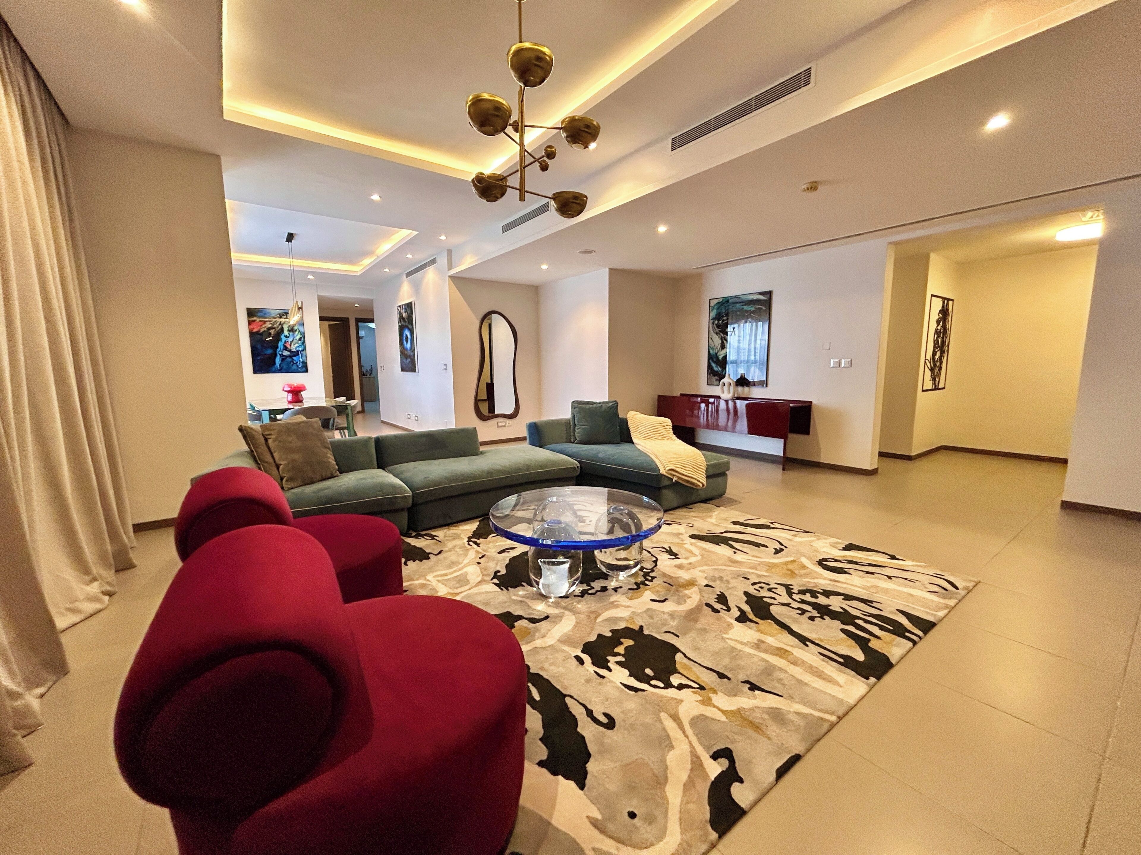 A modern living room with a sofa, red armchairs, a coffee table, and a patterned rug.