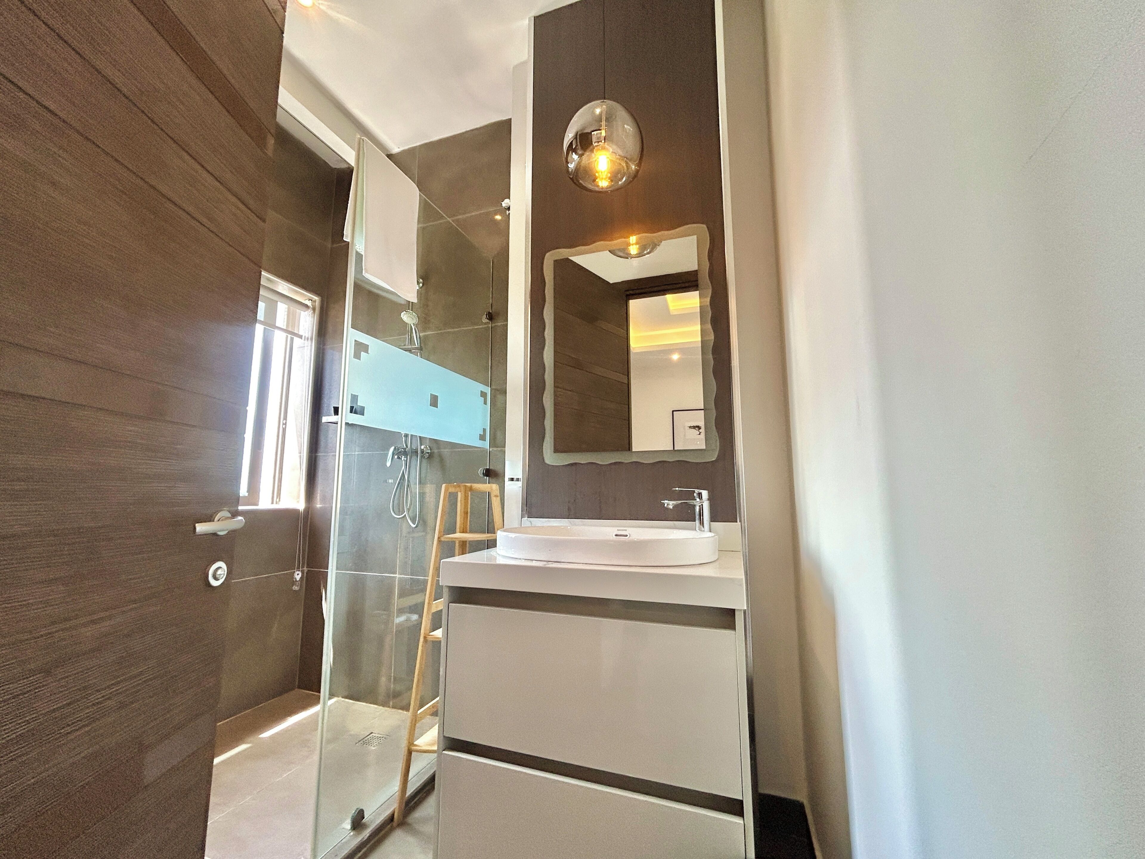 Un baño moderno con cabina de ducha de vidrio, un lavabo blanco y un espejo grande.