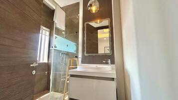 Un baño moderno con cabina de ducha de vidrio, un lavabo blanco y un espejo grande.