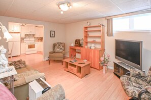 Ein Wohnzimmer mit einer Couch, einem Fernseher, einer Holzkommode und einer Küche im Hintergrund.