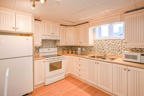 A kitchen with white cabinets, a stove, a microwave, and a sink.