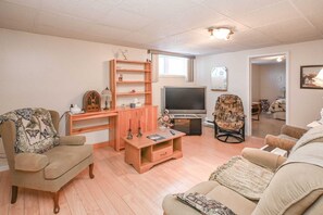A living room with a sofa, armchair, TV, wooden shelves, and a patterned chair.