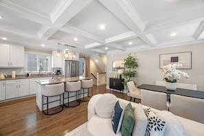 A modern kitchen with bar stools, a dining area with a table and chairs, and a living room with a sofa and decorative pillows. - Union Square Hideaway · Steps to Green Line (Somerville)