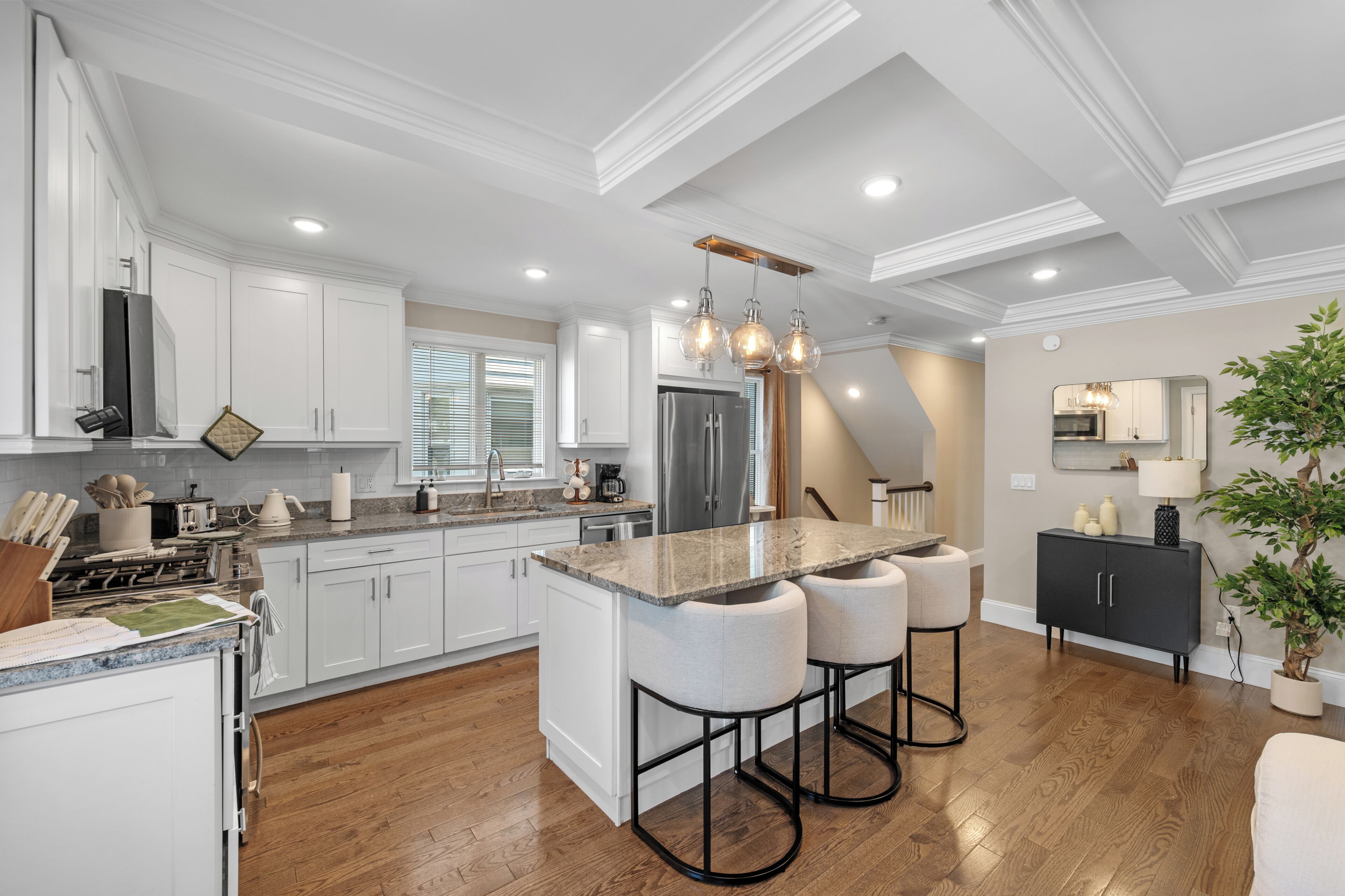 Cocina moderna con armarios blancos, encimera de granito y una isla central con taburetes.