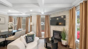 A modern living room with a fireplace, a flat-screen TV mounted above it, and a dining area with a table and chairs.